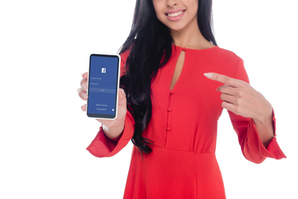 Teilbild einer Frau im roten Kleid, die auf ihr Smartphone zeigt und Facebook isoliert auf Weiß zeigt - Foto, Bild