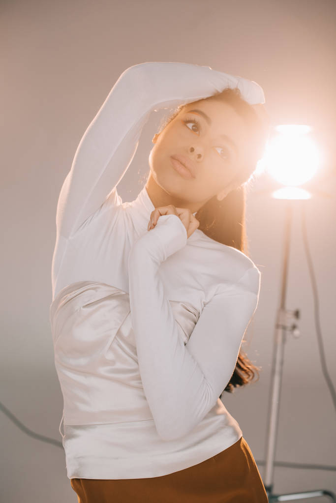 selective focus of african american girl in white turtle neck posing in studio with spotlight - Photo, Image