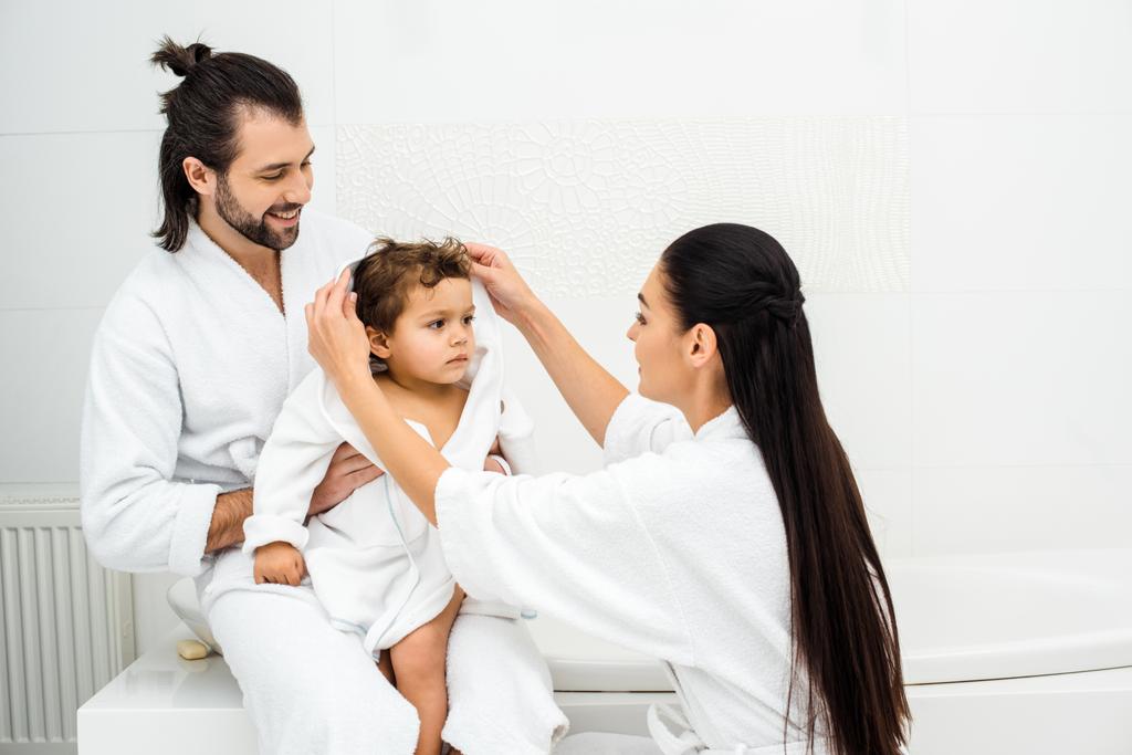 Szülők ül a fürdőszobában kisgyermek fia a fehér fürdőköpeny  - Fotó, kép