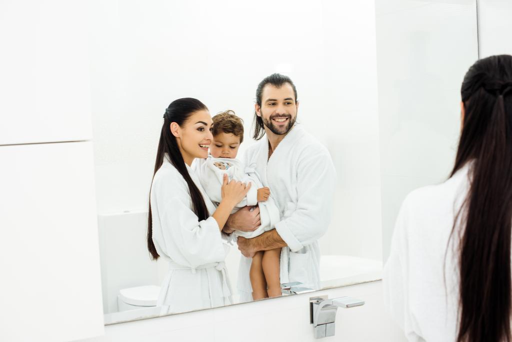 Äiti ja isä katselee peiliin ja pitää lapsi poika valkoinen kylpytakit
  - Valokuva, kuva