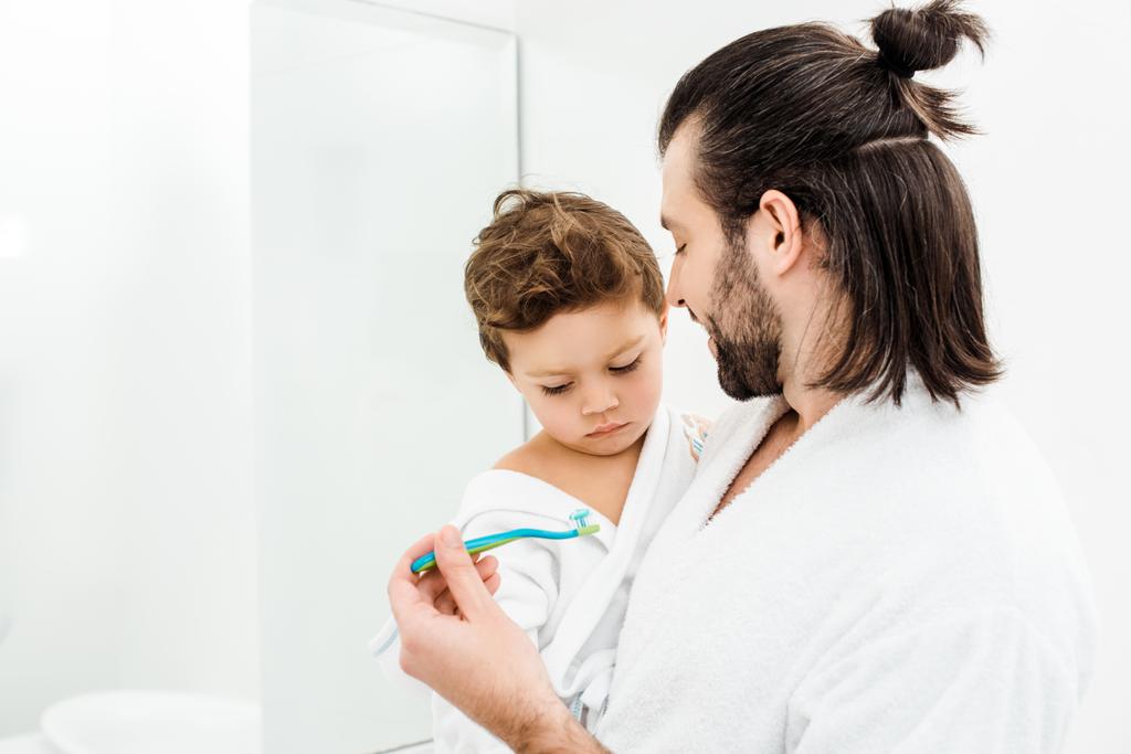 Papa zeigt Kleinkind-Sohn Zahnbürste mit Zahnpasta  - Foto, Bild