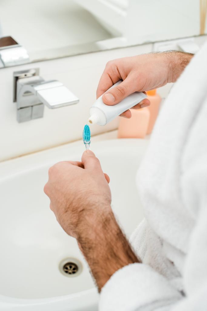 обрізаний вид чоловічих рук додавання зубної пасти на зубну щітку у ванній
 - Фото, зображення