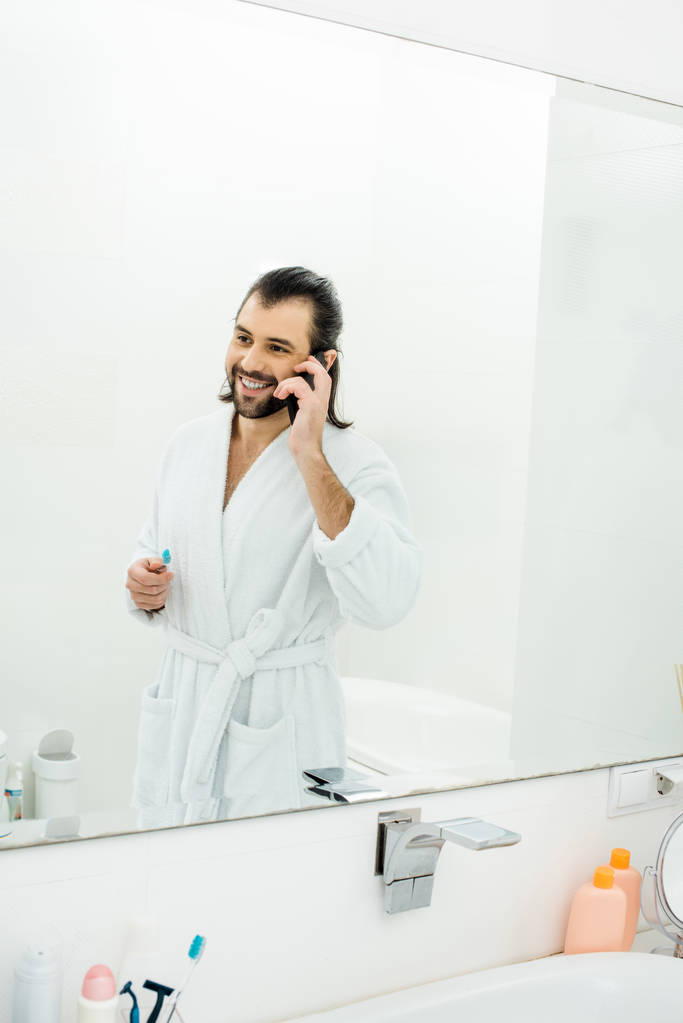 komea aikuinen mies puhuu älypuhelimella ja harjaamalla hampaat kylpyhuoneessa
 - Valokuva, kuva