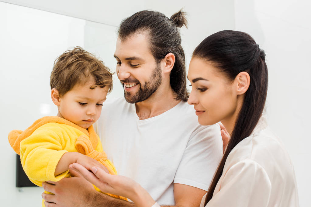 tender young parents holding cute son in yellow bathrobe - Photo, Image