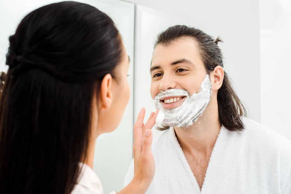 Mujer aplicando espuma de afeitar en la cara sonriente marido
 - Foto, Imagen