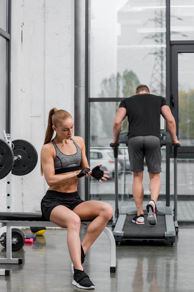 Sportler trainiert auf Laufband, muskulöse Sportlerin trägt Handschuhe für das Training im Fitnessstudio - Foto, Bild