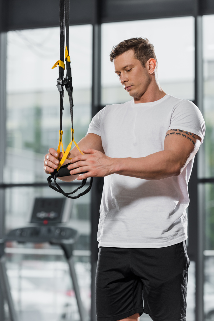 handsome athletic bodybuilder holding suspension straps in gym - Photo, Image