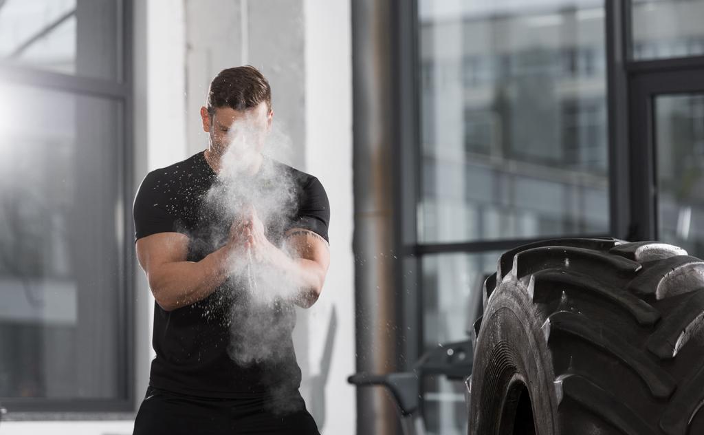 guapo atlético culturista aplicando talco en polvo antes de entrenar con neumático en el gimnasio
 - Foto, Imagen