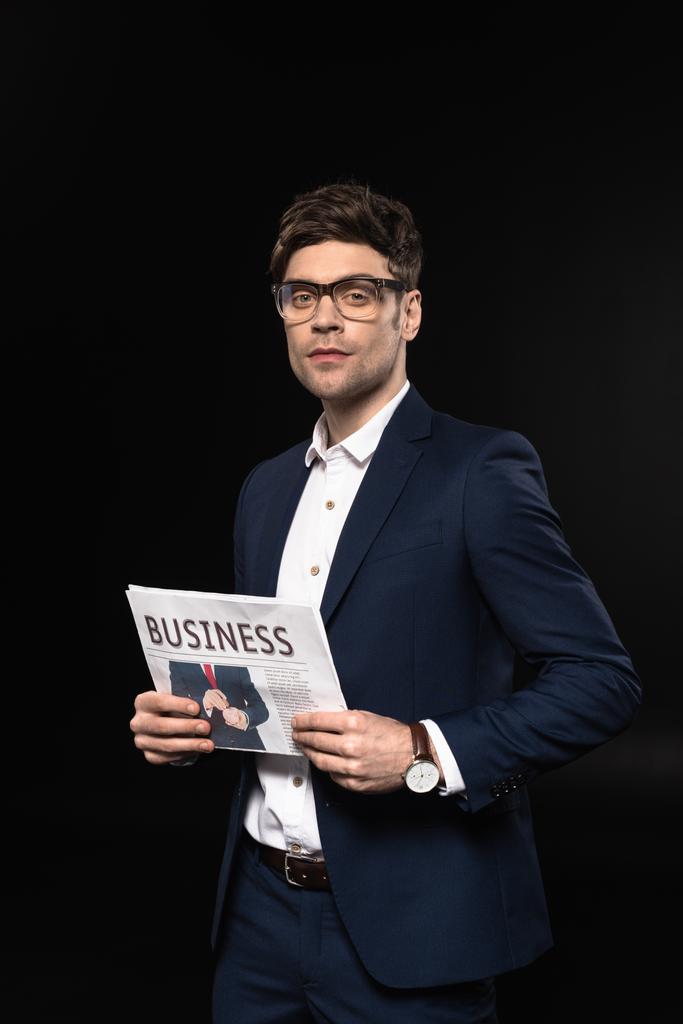 joven hombre de negocios guapo con periódico mirando cámara aislada en negro
 - Foto, imagen