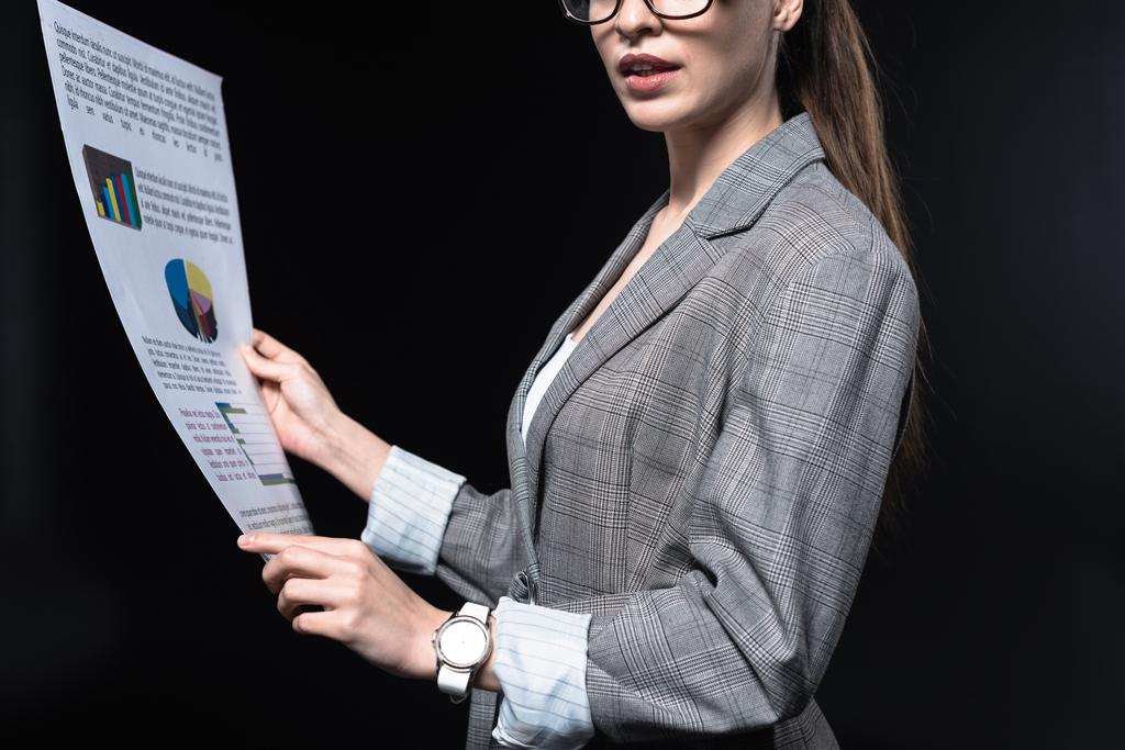 cropped shot of young businesswoman in stylish jacket holding newspaper isolated on black - Photo, Image