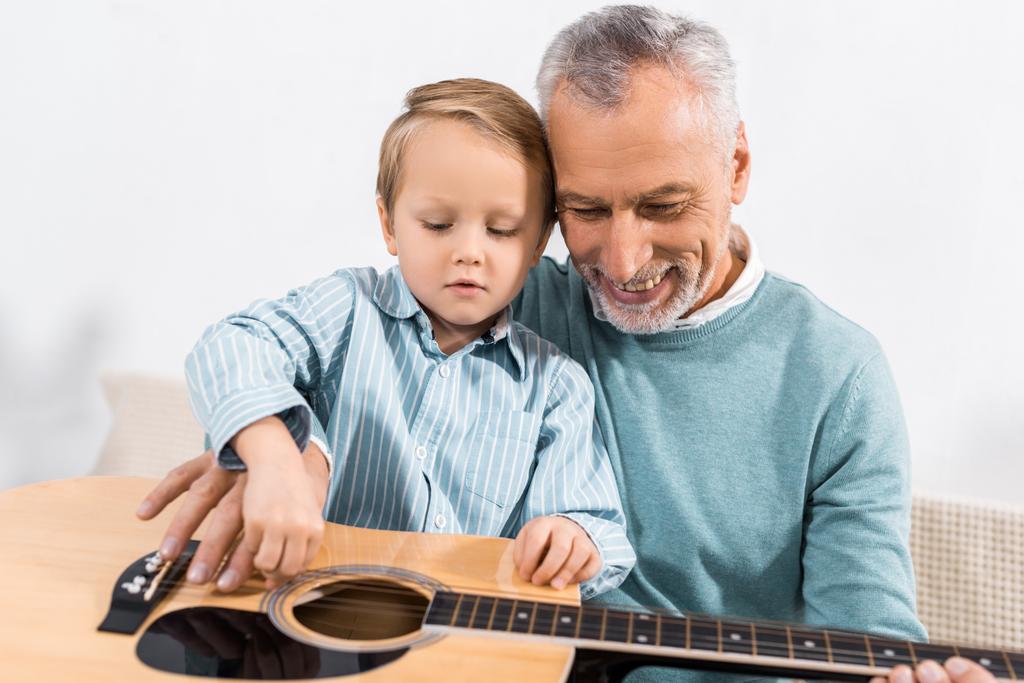 szép nagyapja játszó unokája térdre játszik akusztikus gitár otthon - Fotó, kép