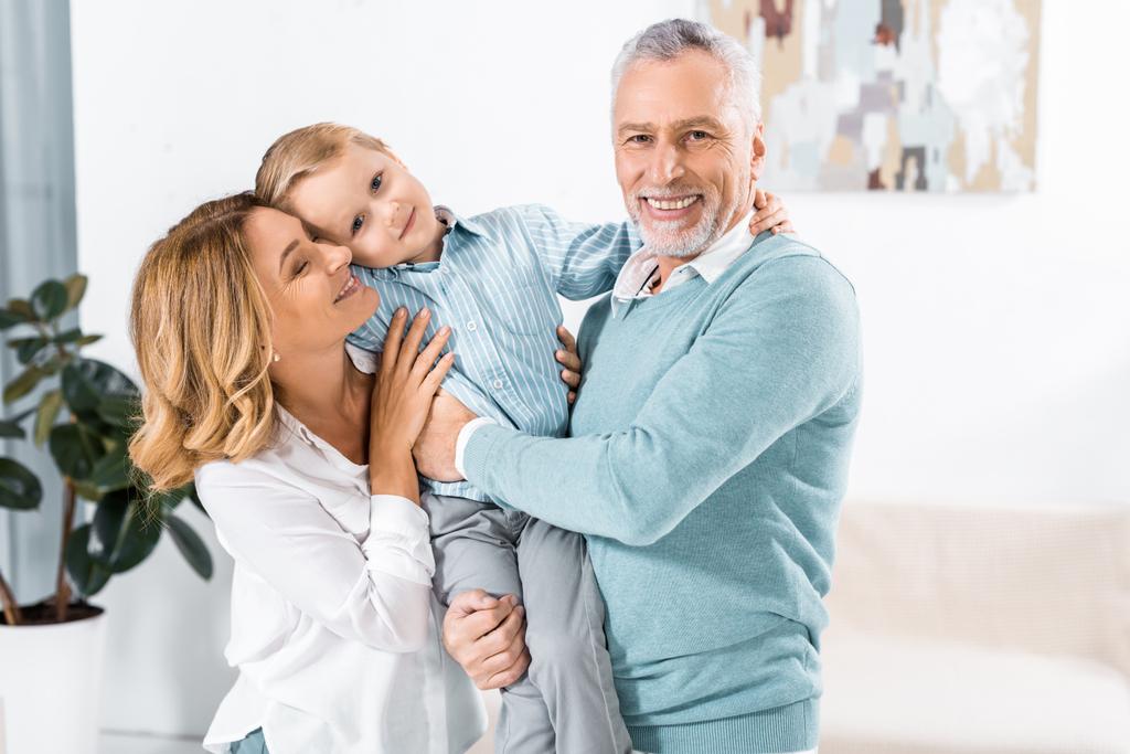 laughing mature couple holding adorable grandson at home - Photo, Image