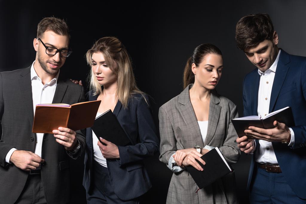 group of serious business people reading notebooks together isolated on black - Photo, Image