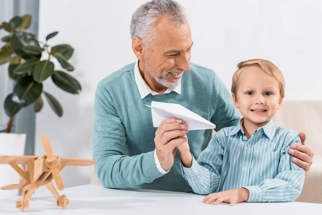 heureux grand-père et adorable petit-fils s'amuser avec avion en papier à la maison
 - Photo, image