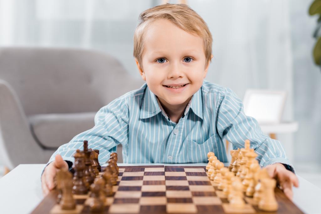 retrato de niño feliz mirando la cámara cerca del tablero de ajedrez en casa
 - Foto, imagen