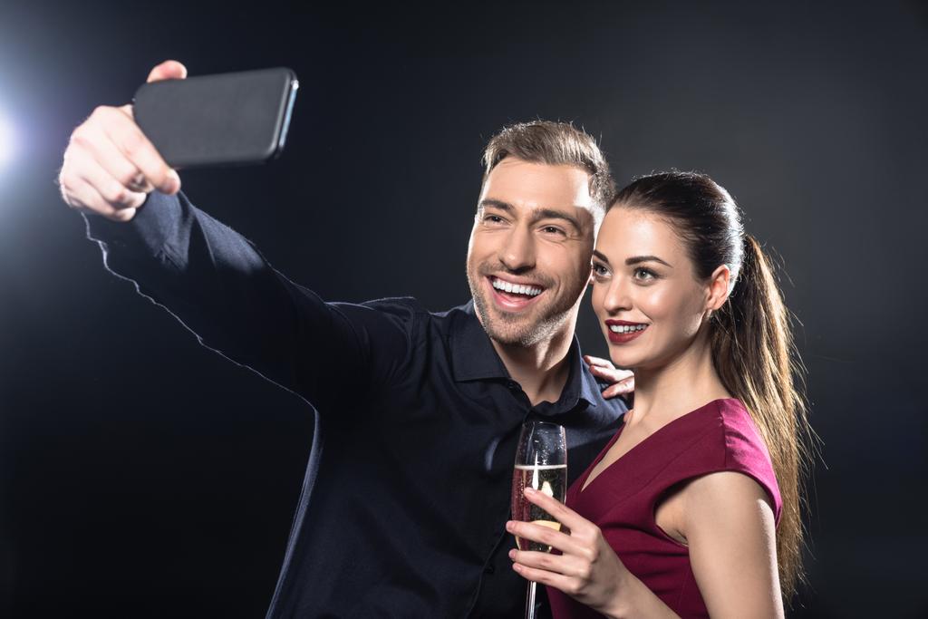 glückliches junges Paar macht Selfie mit Smartphone bei Party auf schwarz - Foto, Bild