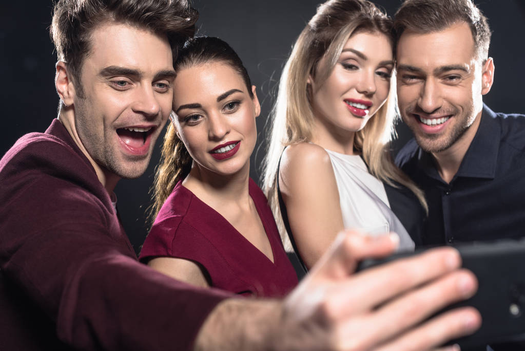 Close-up shot skupiny přátel, přičemž selfie s smartphone během party na černém pozadí - Fotografie, Obrázek