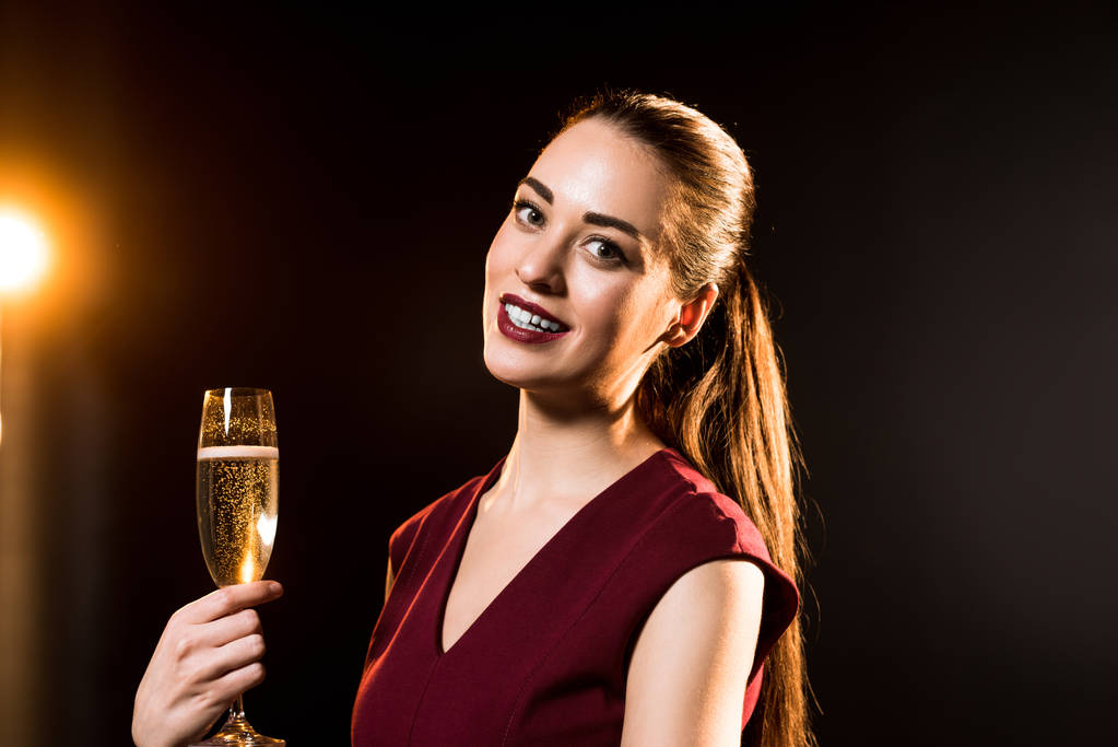 uśmiechnięta młoda kobieta trzyma kieliszek szampana na czarny - Zdjęcie, obraz