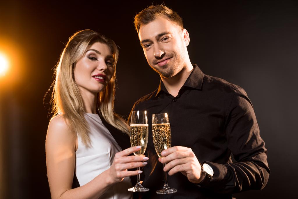 щаслива молода пара в келихах шампанського стоїть разом на чорному і дивиться на камеру
 - Фото, зображення