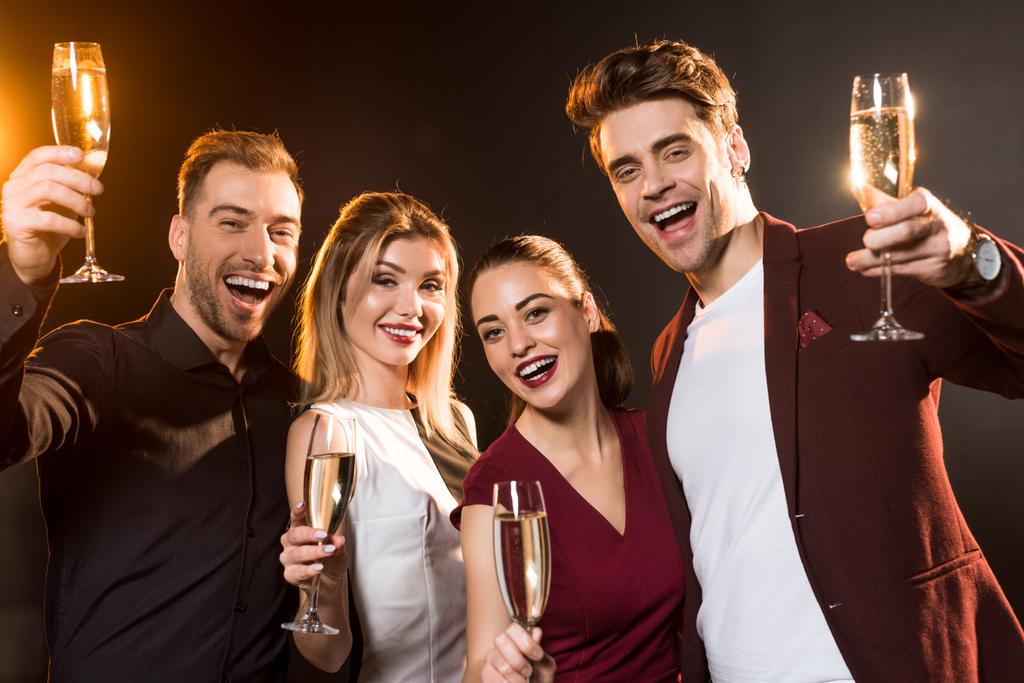 groep vrienden houden glazen champagne en camera kijken tijdens party op zwart - Foto, afbeelding