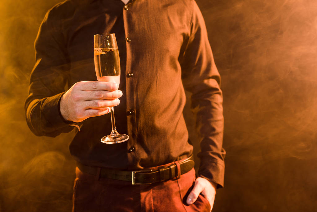 cropped shot of man with glass of champagne under yellow light on black - Photo, Image