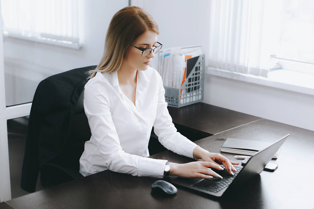 Cálmate mujer rubia atractiva joven seria utiliza el ordenador portátil para trabajar en la mesa en la oficina. Retrato de negocios. Proceso de trabajo
 - Foto, imagen