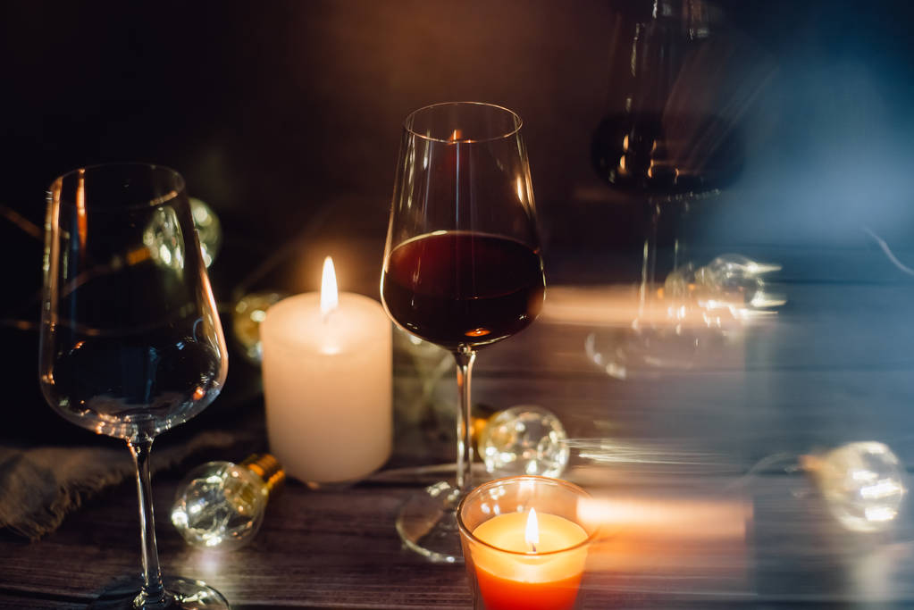 Composición festiva hecha de copa de vino tinto, velas y guirnaldas sobre un fondo oscuro
 - Foto, imagen