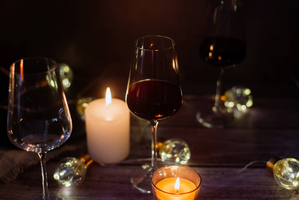 Samenstelling van de vakantie gemaakt van glas rode wijn, kaarsen en slingers op een donkere achtergrond - Foto, afbeelding