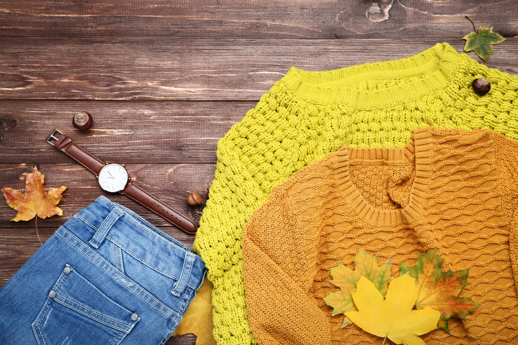 Suéteres de punto con jeans y hojas de arce sobre mesa de madera marrón
 - Foto, imagen