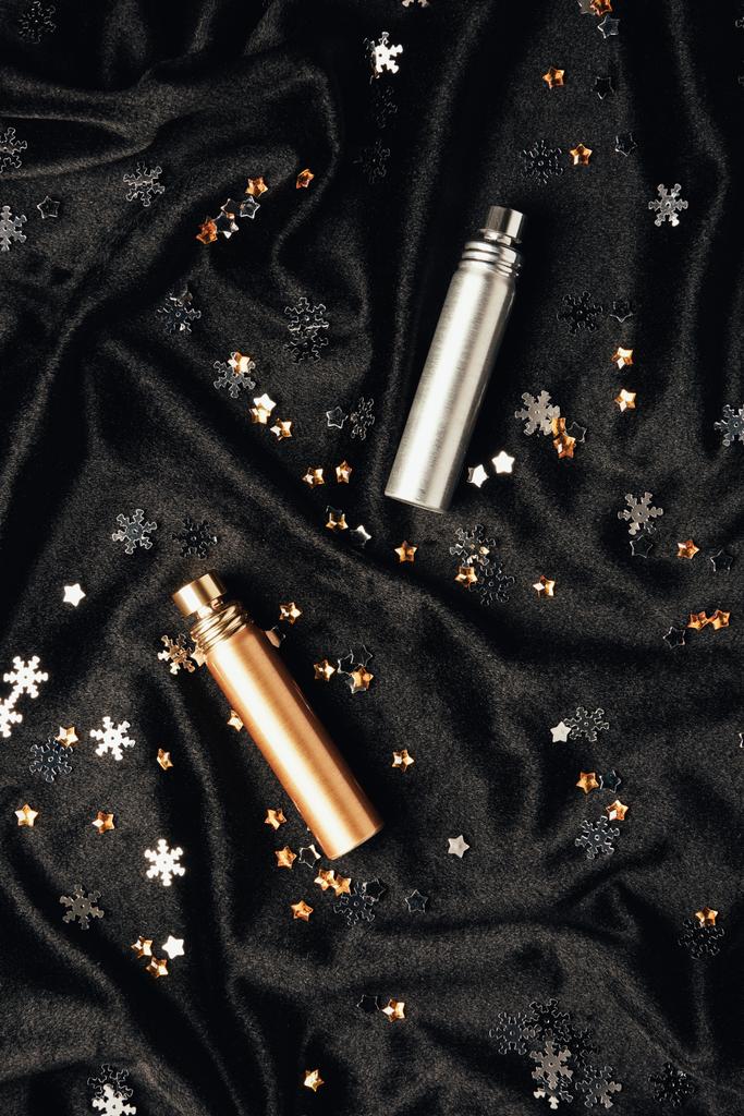 vue de dessus des parfums et des flocons de neige décoratifs brillants sur tissu noir
 - Photo, image
