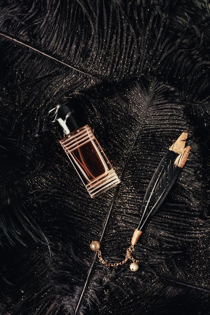 vista superior de la botella de perfume y plumas negras decorativas con polvo dorado
 - Foto, imagen