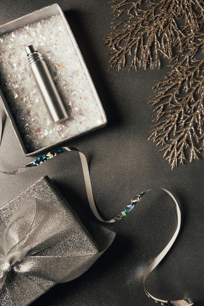 vista superior de la botella de perfume en caja de regalo, cinta de plata y ramitas decorativas brillantes en gris
 - Foto, Imagen