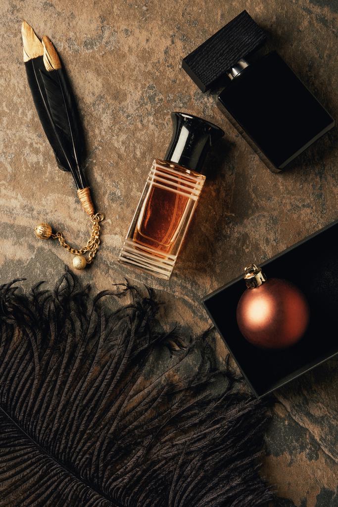 top view of perfumes, decorative black feathers and shiny christmas ball - Photo, Image