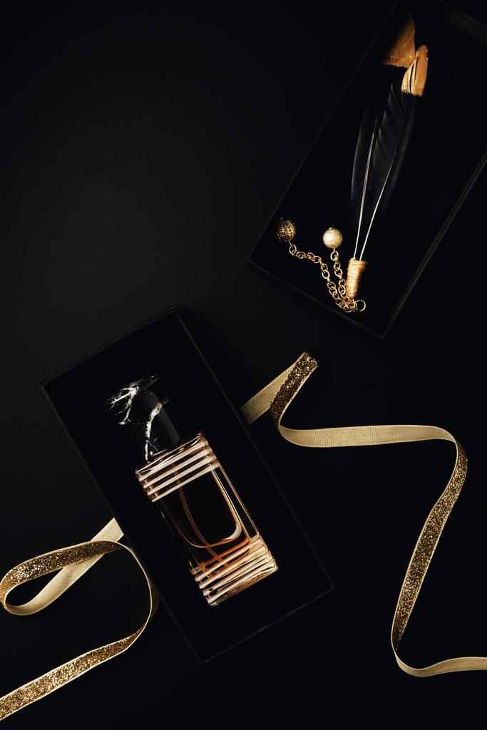pohled shora parfému láhve s zlatá stuha, krabičky a dekorační peří na černém pozadí - Fotografie, Obrázek