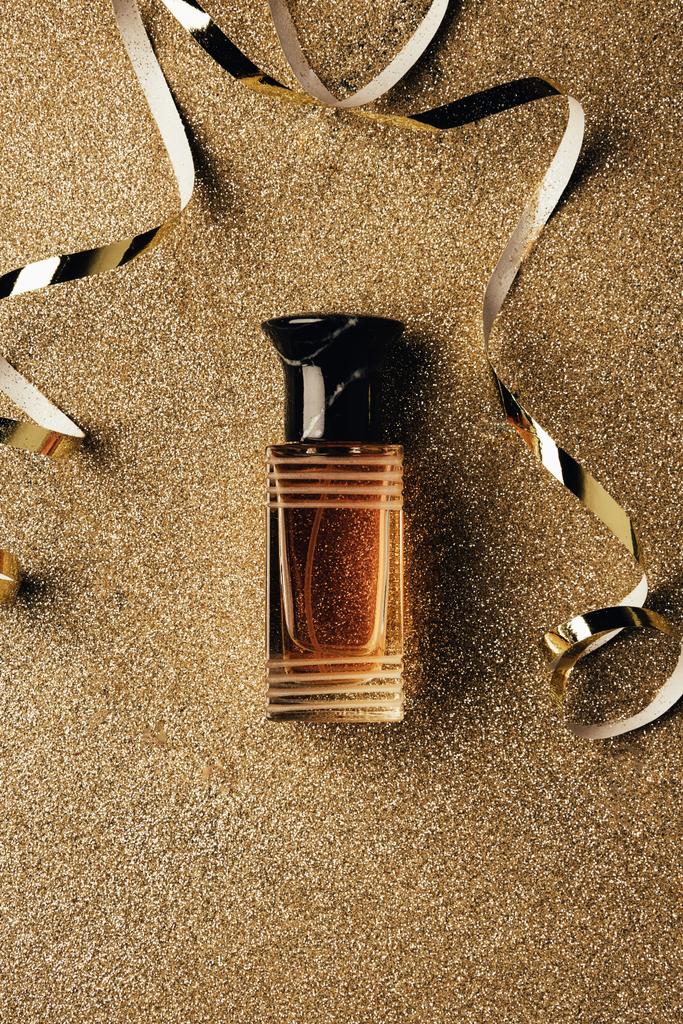 vista superior da garrafa de perfume e fitas douradas na superfície brilhante
 - Foto, Imagem