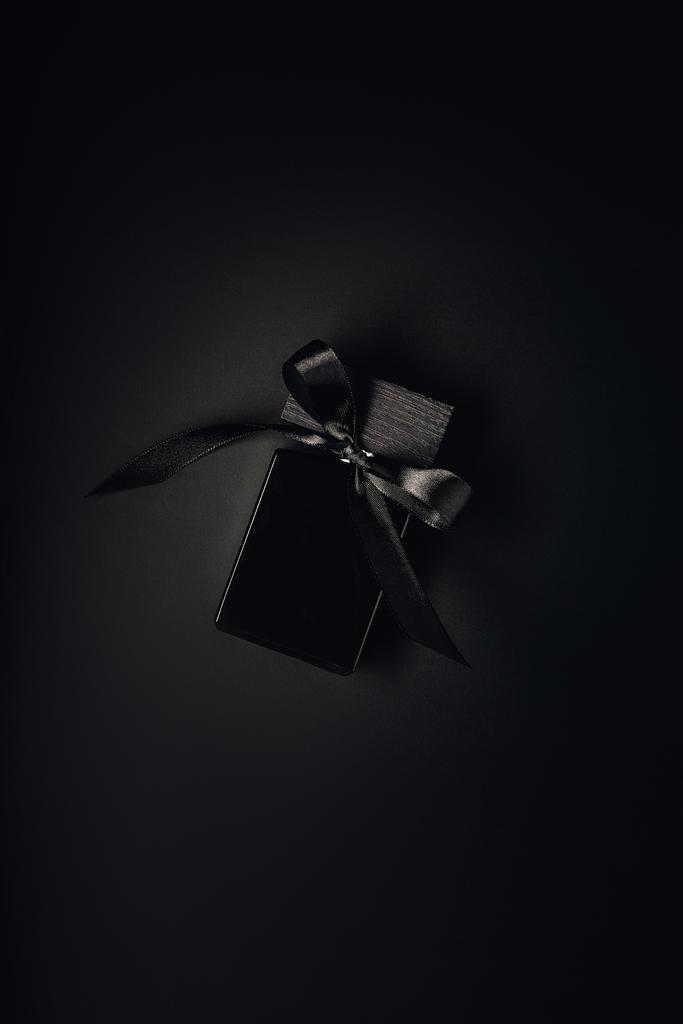 κάτοψη του μαύρου Άρωμα μπουκάλι με κορδέλα σε μαύρο φόντο - Φωτογραφία, εικόνα