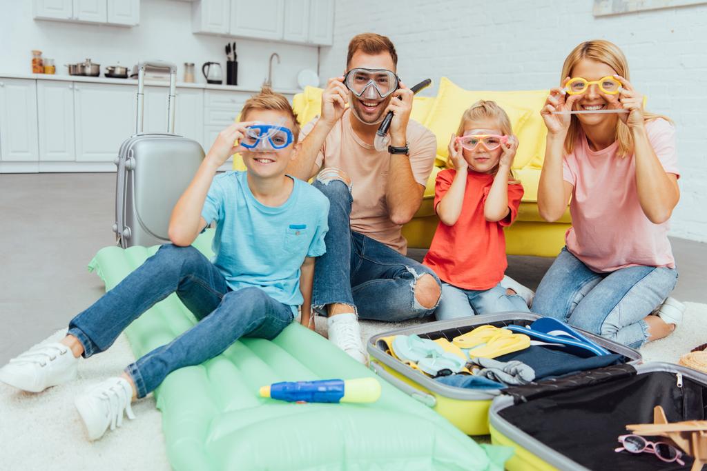 família feliz em máscaras de natação olhando para a câmera e posando enquanto faz as malas para férias de verão, conceito de viagem
 - Foto, Imagem