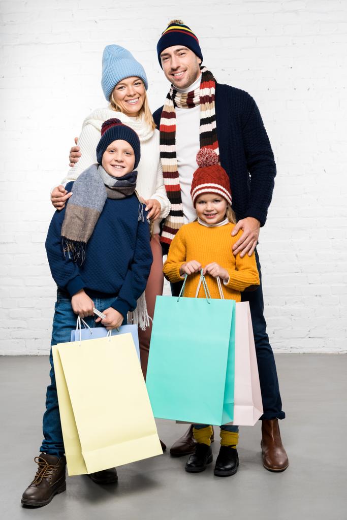 Szczęśliwa rodzina w zimowe ubrania patrząc na kamery i trzymając torby na zakupy - Zdjęcie, obraz