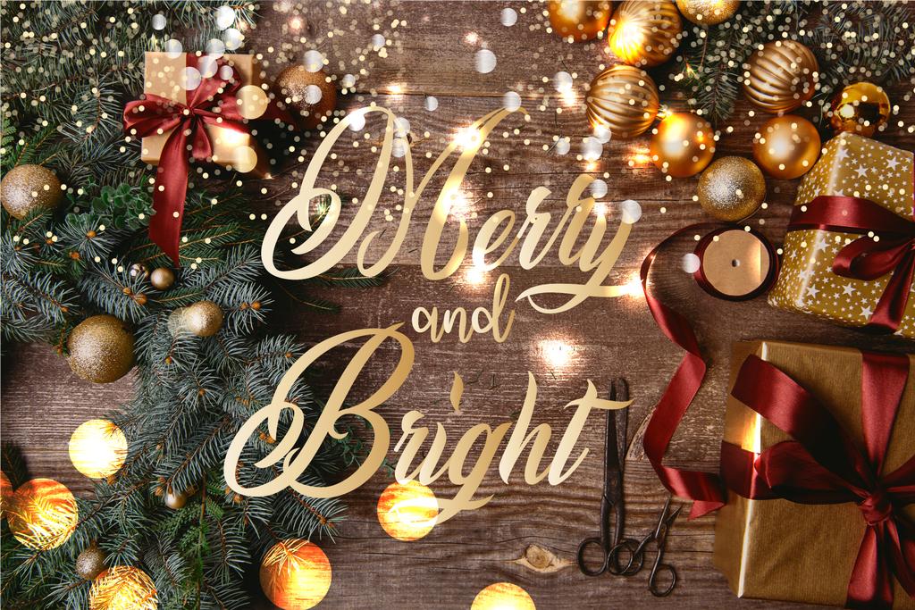 verhoogde weergave van kerst geschenkdozen, fir krans, spool lint en schaar op houten tafel met "vrolijk en heldere" belettering en gloeiende lichten - Foto, afbeelding