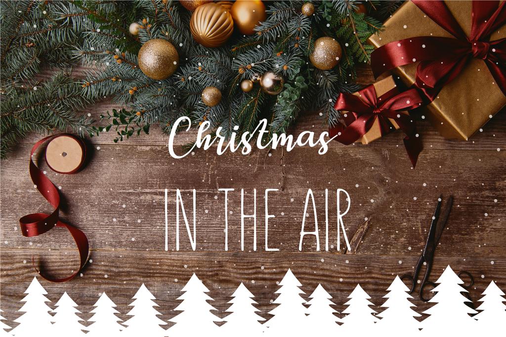 bovenaanzicht van kerst geschenkdozen, fir krans, spool lint en schaar op houten tafel met "christmas in de lucht" inspiratie, sneeuw en kerst bomen illustratie - Foto, afbeelding
