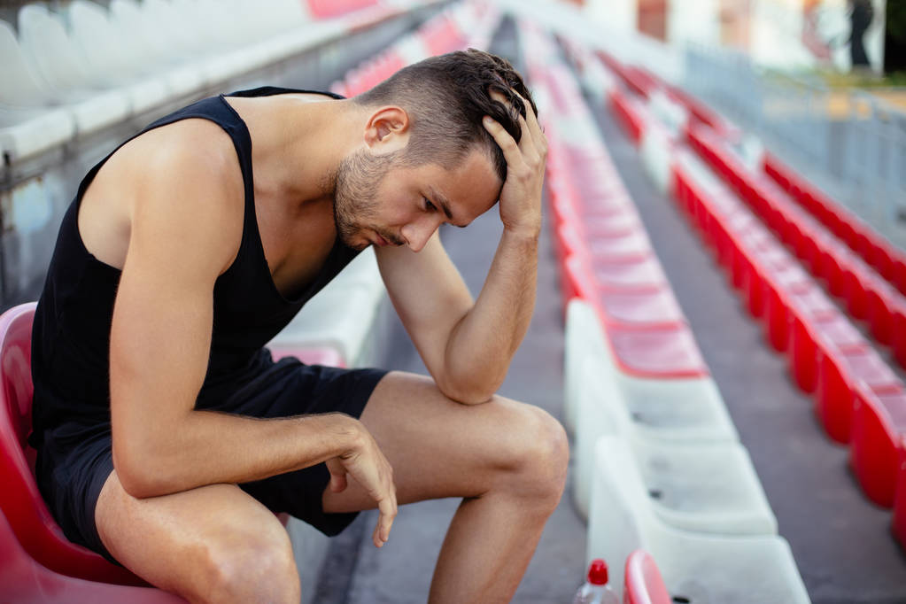 Depressed athlete man sitting head in hands on stadium seats, stress and sad concept - Photo, Image