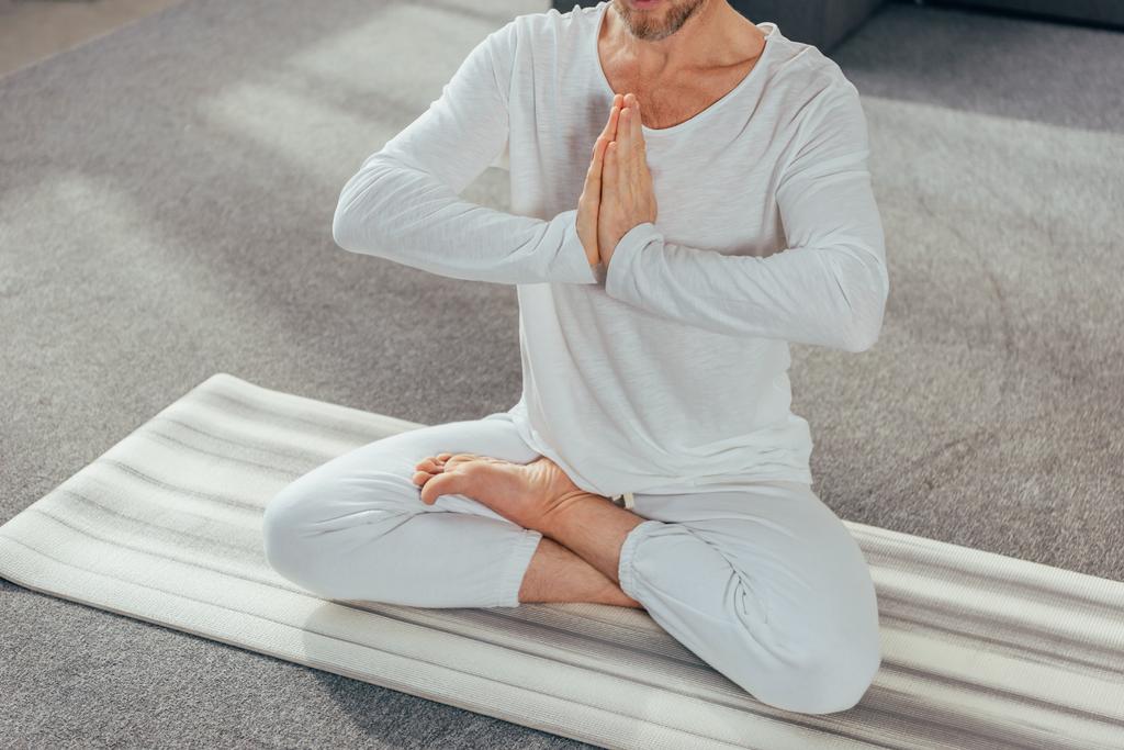 cropped shot of man sitting in lotus position and meditating with namaste gesture on yoga mat - Photo, Image
