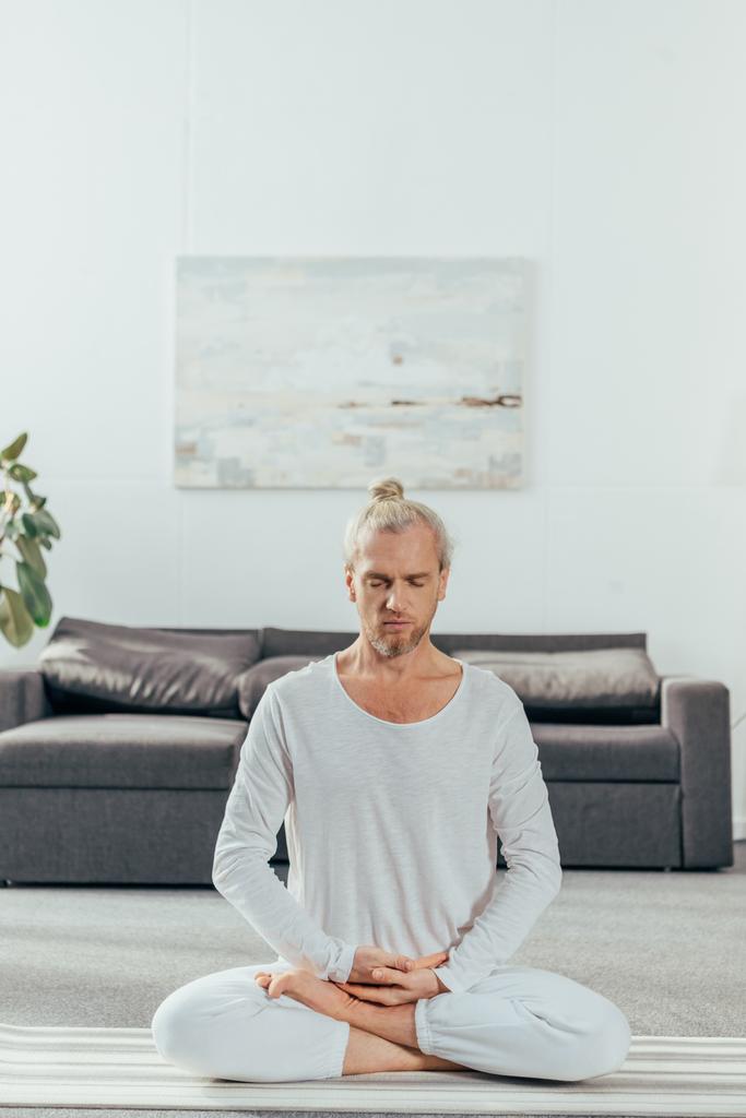 flexibler erwachsener Mann meditiert zu Hause in Lotusposition auf Yogamatte  - Foto, Bild