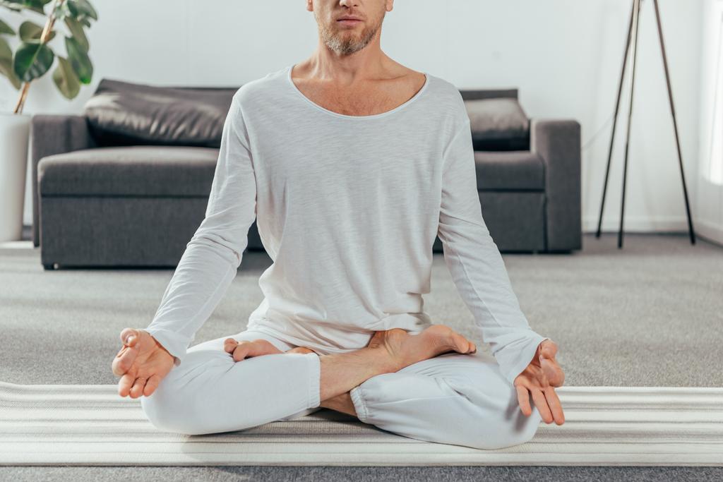tiro cortado de homem em sportswear meditando no tapete de ioga em casa
 - Foto, Imagem