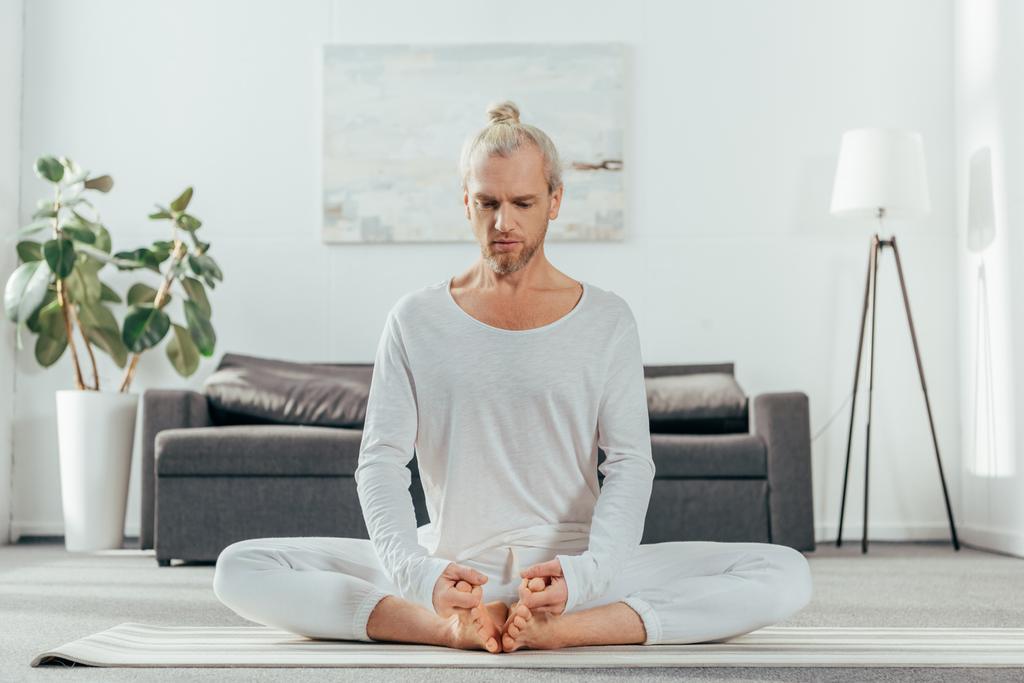 homme méditant en position lotus sur tapis de yoga à la maison
 - Photo, image