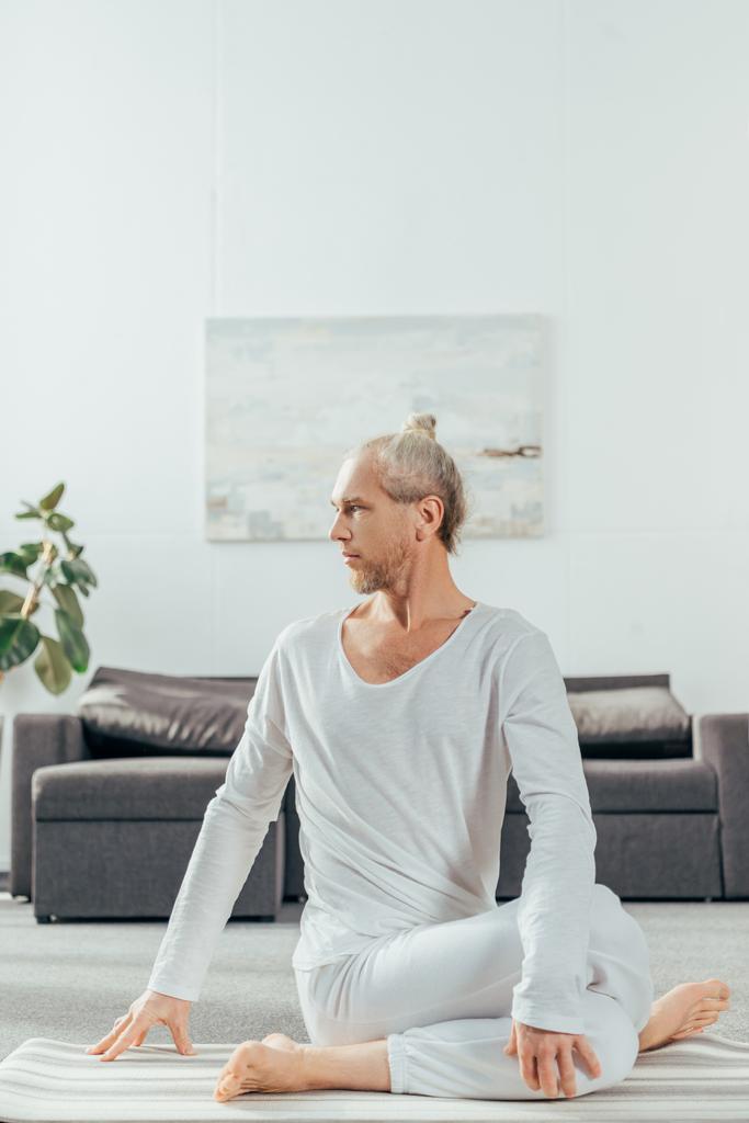 adulto sportivo uomo seduto in mucca faccia posa su tappetino yoga e guardando lontano a casa
 - Foto, immagini