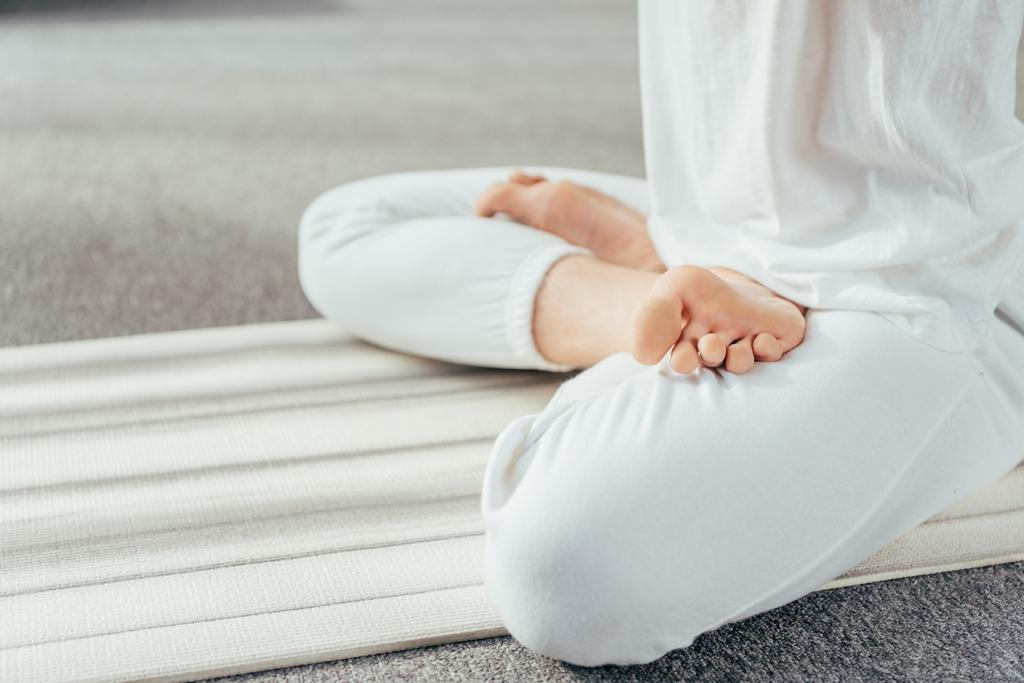 ritagliato colpo di uomo meditando in posizione loto sul tappetino yoga a casa
 - Foto, immagini