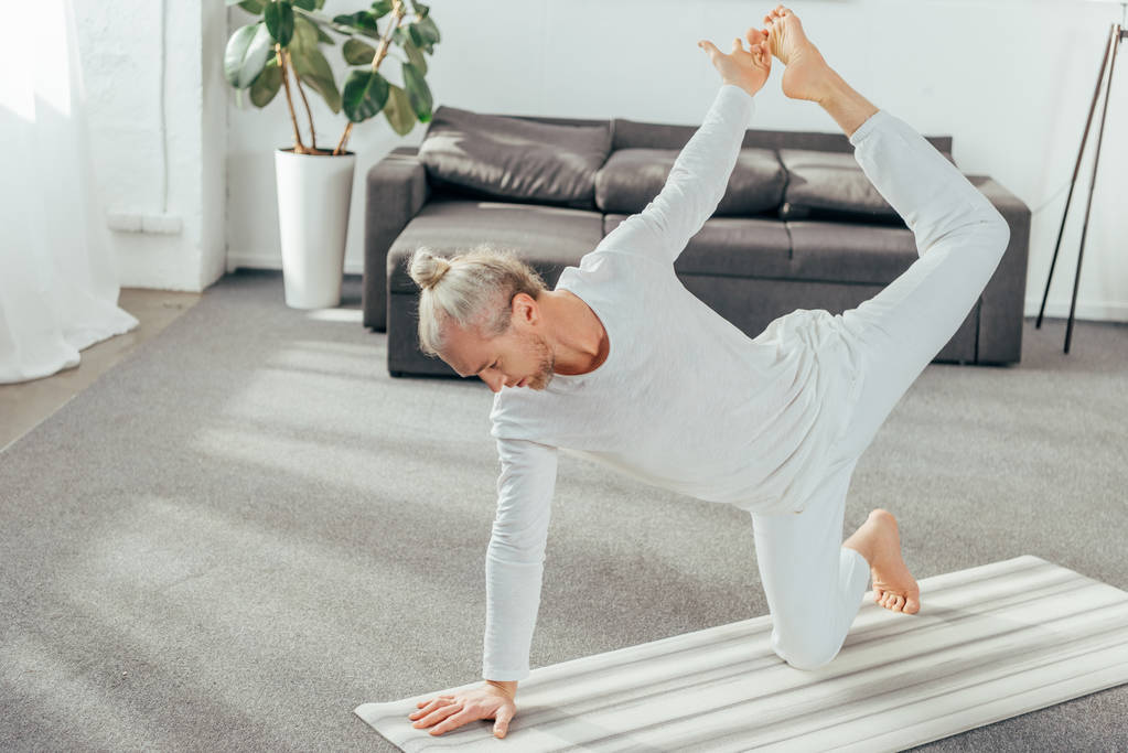hoge hoekmening van flexibele volwassen mens yoga oefenen op mat thuis - Foto, afbeelding