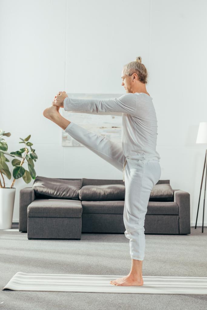 Seitenansicht eines barfuß erwachsenen Mannes, der zu Hause Yoga praktiziert - Foto, Bild