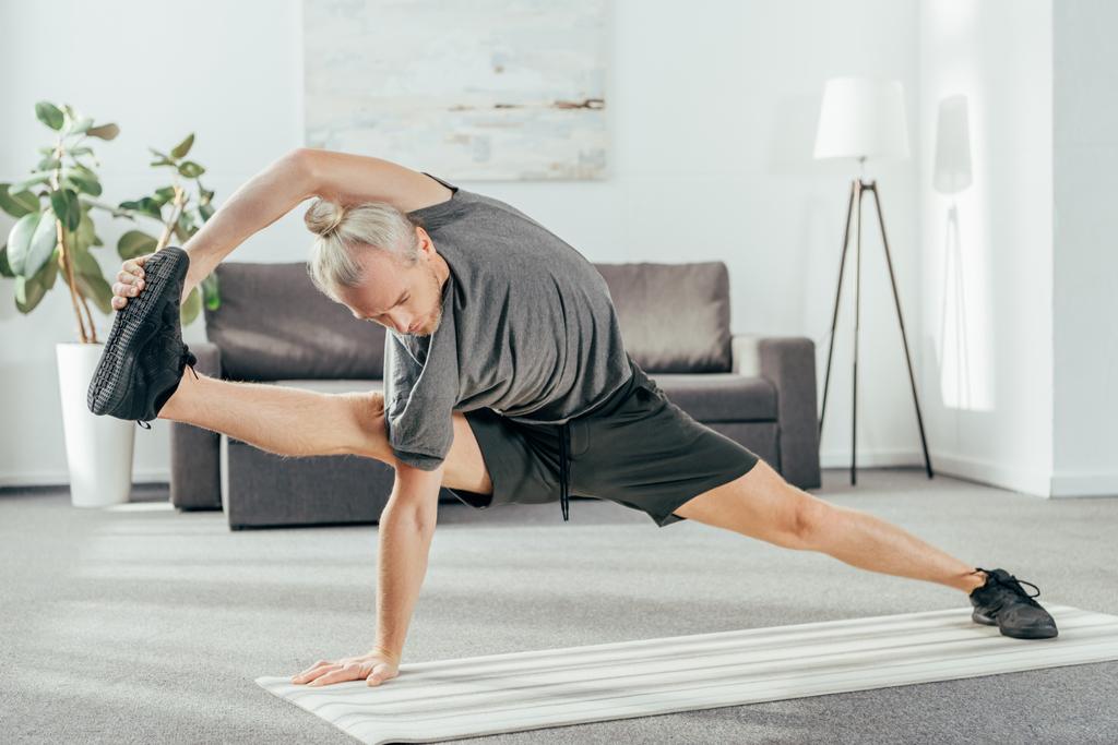 sportowy dorosły człowiek równoważenia i rozciąganie na matę do jogi w domu  - Zdjęcie, obraz